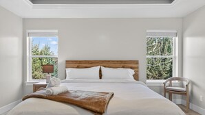A bedroom with a wooden headboard, white bedding, and a view of trees through large windows. - Nampa`s New Nest - The Orion (Nampa)