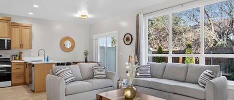 A modern living room with a grey sofa, wooden coffee table, and a large window offering a view of trees.