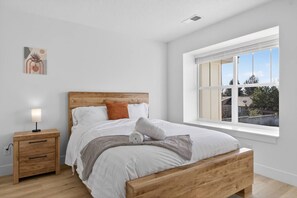 Una camera da letto con un letto in legno, biancheria da letto bianca, un comodino con una lampada e una finestra vista esterna.