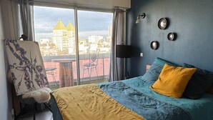 A bedroom with a bed, a chair, and a view of a cityscape through large windows. - Lovely 3-room apartment with swimming pool in Puteaux (Puteaux)