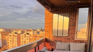A balcony with a green artificial turf floor, a wooden bench, a cushioned sofa, and a small table with a mushroom-shaped top. - Lovely 3-room apartment with swimming pool in Puteaux (Puteaux)