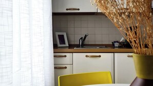 Una cocina con armarios blancos, una silla amarilla y un jarrón con flores secas sobre la mesa.