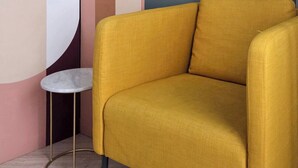 Un sillón amarillo en una habitación con diseño moderno, que incluye una mesa redonda y arte abstracto en la pared.