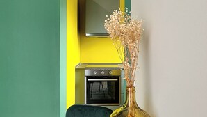 Ein Zimmer mit einem schwarzen Tisch, einer Vase mit getrockneten Blumen, einer gelben Wand und einer Küchenzeile mit einem Backofen.