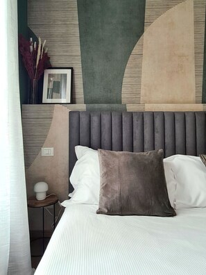 A neatly arranged bedroom with a bed, pillows, a bedside table with a lamp, and a wall with abstract art and a switch. - deluxe apartment (Milan)