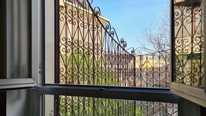 Ein Fenster mit Metallgeländer und Blick auf Gebäude und Grünflächen.