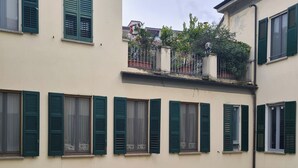 A multi-story building with green shutters on windows, a balcony with plants, and a chimney. - Serendipity Apartments Missori (Milan)