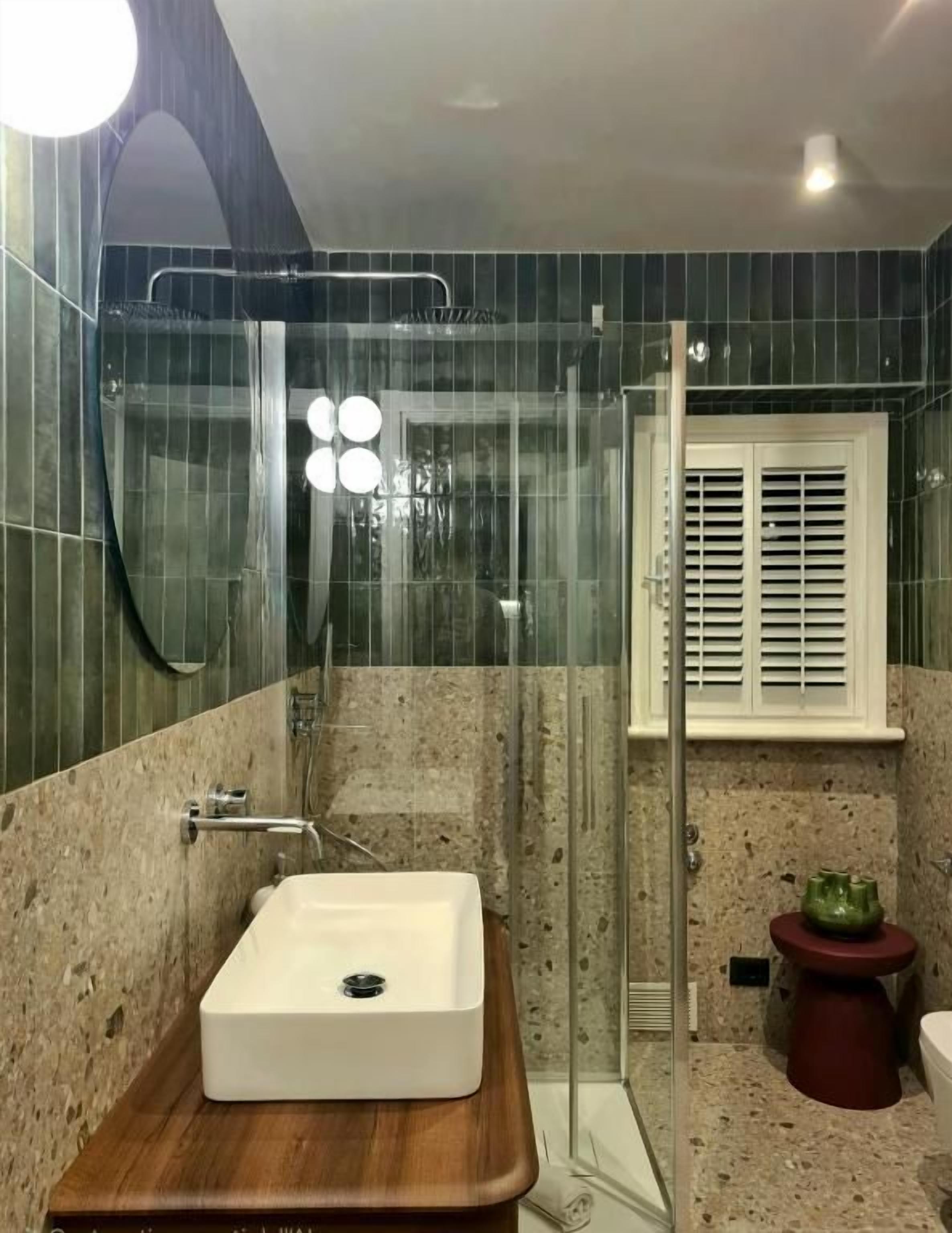 Un baño con cabina de ducha de vidrio, un lavamanos blanco y un taburete rojo.