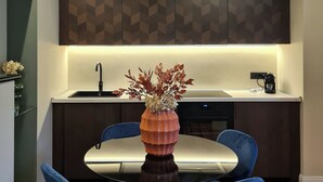 A modern kitchen with a dining area. It includes a kitchen island with a sink, a coffee maker, and a vase with flowers. There are four blue chairs around the dining table. - Serendipity Apartments Missori (Milan)