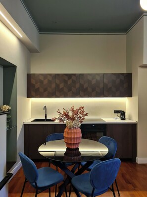 A modern kitchen with a dining area. It includes a kitchen island with a sink, a coffee maker, and a vase with flowers. There are four blue chairs around the dining table. - Serendipity Apartments Missori (Milan)
