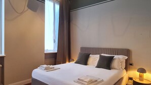 A neatly made bed with pillows and folded towels, a bedside lamp, and a window with curtains. - Serendipity Apartments Missori (Milan)