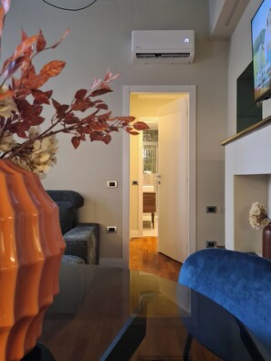 A modern living room with a blue sofa, a decorative orange vase, and an air conditioning unit on the wall. - Serendipity Apartments Missori (Milan)