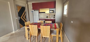 A compact kitchen with a refrigerator, microwave, and sink. There is a dining table with chairs and a patterned tablecloth.