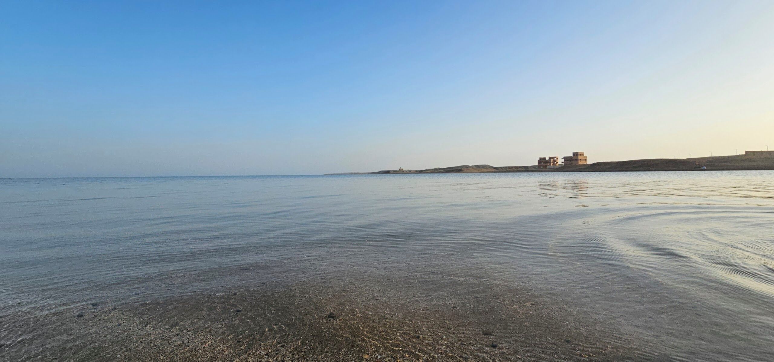 A beach with calm waters and a distant building with multiple levels.