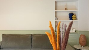 Een woonkamer met een bank, een ronde tafel en een vaas met gedroogde planten.