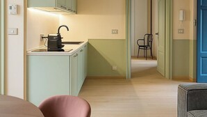 Een moderne keuken met lichtgroene kastjes, een zwarte waterkoker en een houten eettafel met twee stoelen.