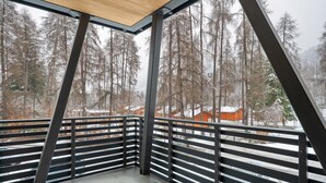 Un coin de balcon avec des garde-corps en métal, un sol en béton et une vue sur des arbres et des bâtiments recouverts de neige.