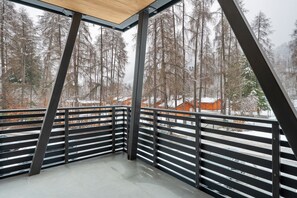 Ein Balkoneck mit Metallgeländern, einem Betonboden und Blick auf schneebedeckte Bäume und Gebäude.