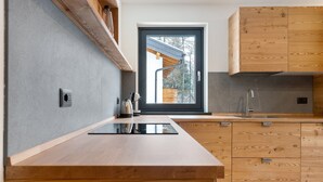 Une cuisine moderne avec des meubles en bois, une cuisinière encastrée et une fenêtre donnant sur une structure en bois à l’extérieur.