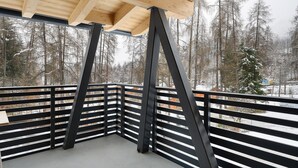 Un balcone con soffitto in legno e ringhiere metalliche, con vista su una foresta innevata.