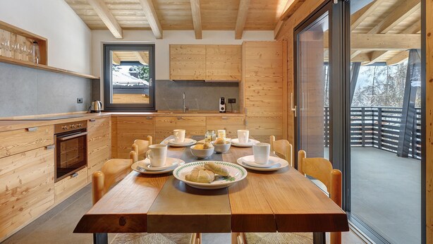Una cucina moderna con mobili in legno, un tavolo da pranzo apparecchiato con piatti, tazze e una ciotola di cibo.