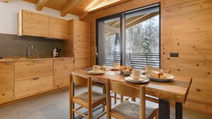 Ambiente interno in legno con angolo cottura e zona pranzo, caratterizzato da armadietti, un tavolo apparecchiato con piatti, tazze e una ciotola di frutta.