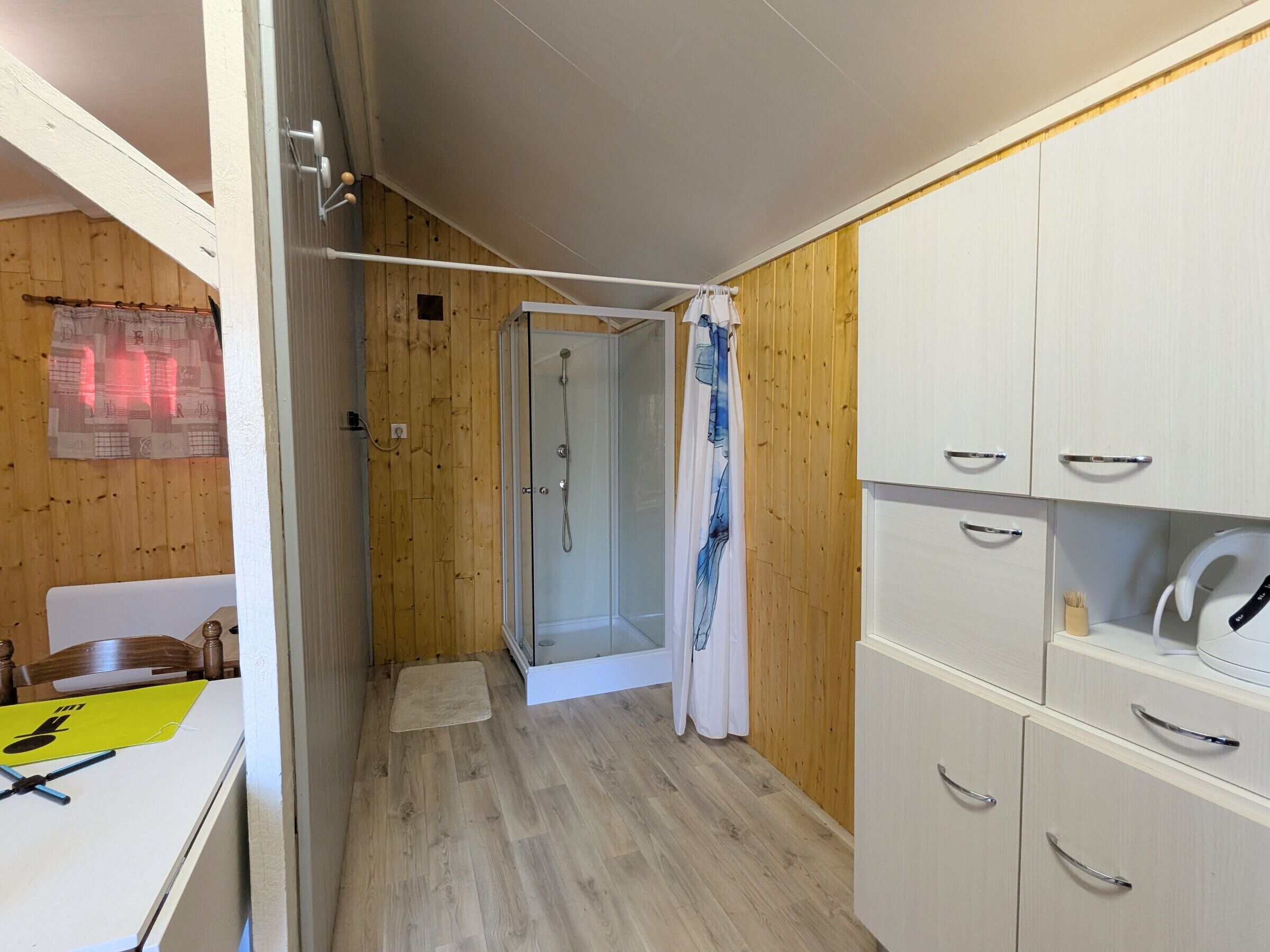 Un baño pequeño con ducha, paredes de madera y muebles blancos.