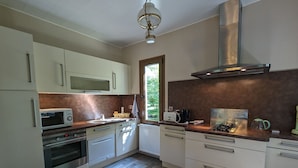 A modern kitchen with white cabinets, a built-in microwave, a gas stove, and a window with a view of greenery. - Private island in Berry - Riverside paradise (Le Menoux)
