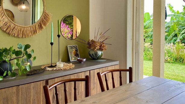 A dining area with a wooden table and chairs, a mirror, and a vase with dried flowers. - Cozy cottage, mountain view - 4 guests (Le Tampon)