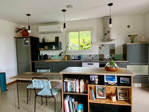 A modern kitchen with a dining area, a built-in bookshelf, and a window with a view of greenery.