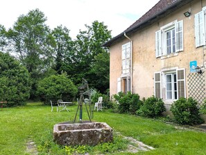 Une maison de campagne avec un jardin, un puits en pierre et une sculpture en métal.