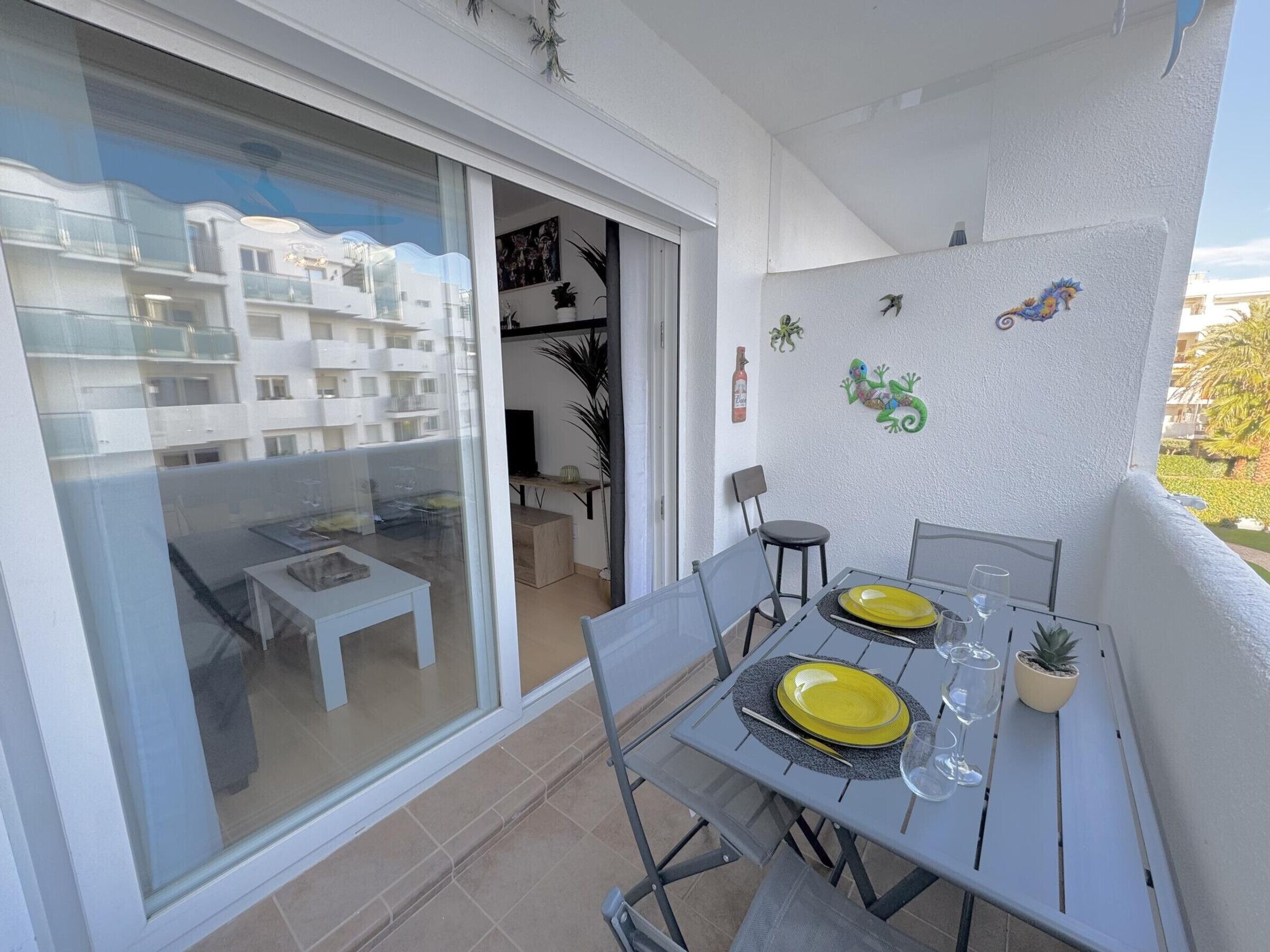 Un balcone con un tavolo da pranzo per due persone, una porta scorrevole in vetro e vista su un edificio residenziale.