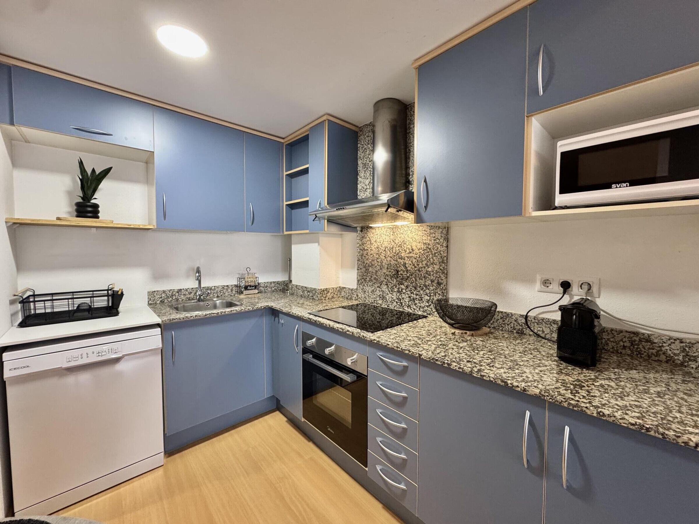 Una cocina moderna con armarios azules, encimera de granito, microondas integrado y lavavajillas.