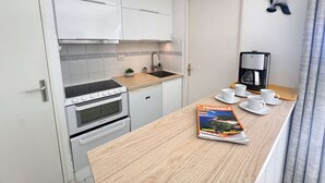 Una cucina compatta con mobili bianchi, un fornello e una macchina da caffè. Una rivista intitolata 'Provence' è sul bancone.