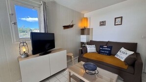 Un soggiorno moderno con una TV su un mobile bianco, un divano marrone con cuscini decorativi, un tavolino e una finestra con tende.