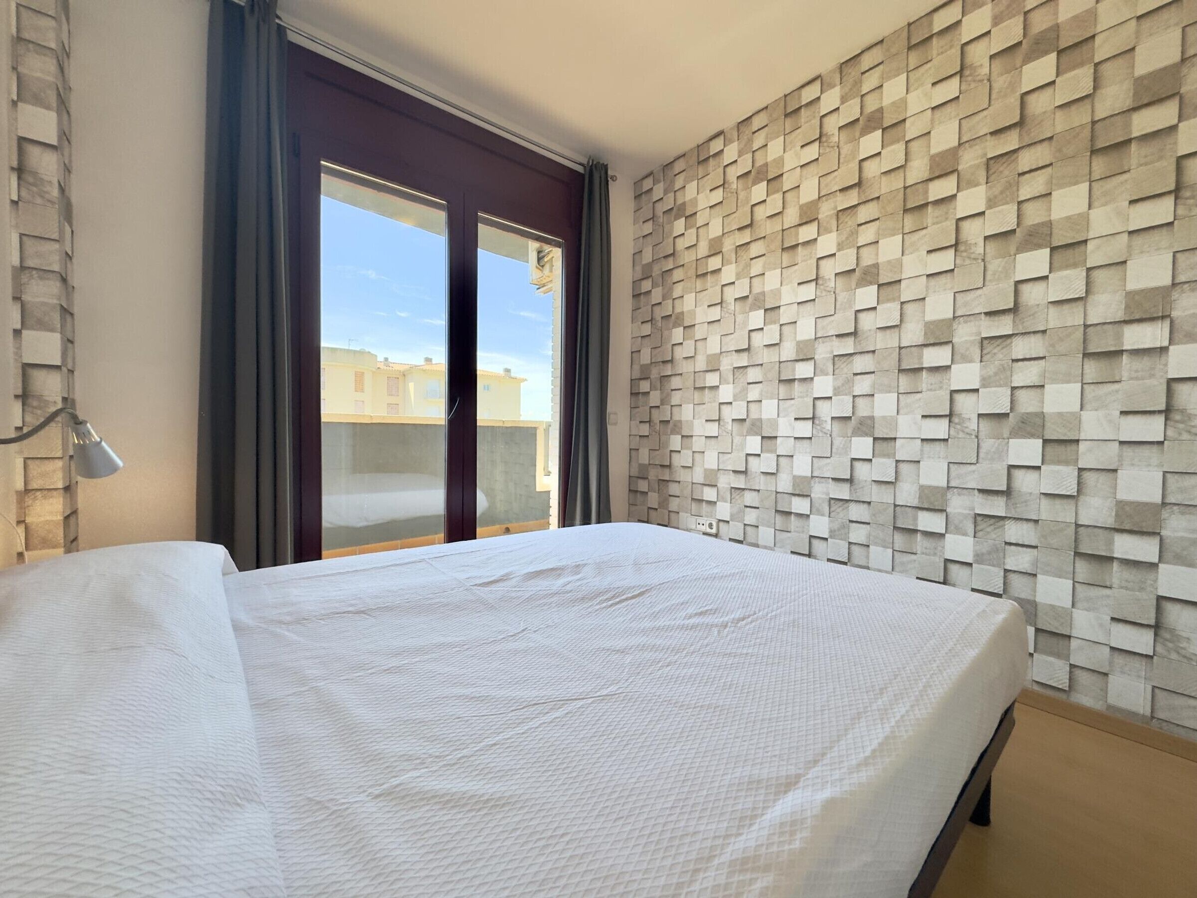 A hotel room with a bed, a window, and a wall with a geometric pattern.