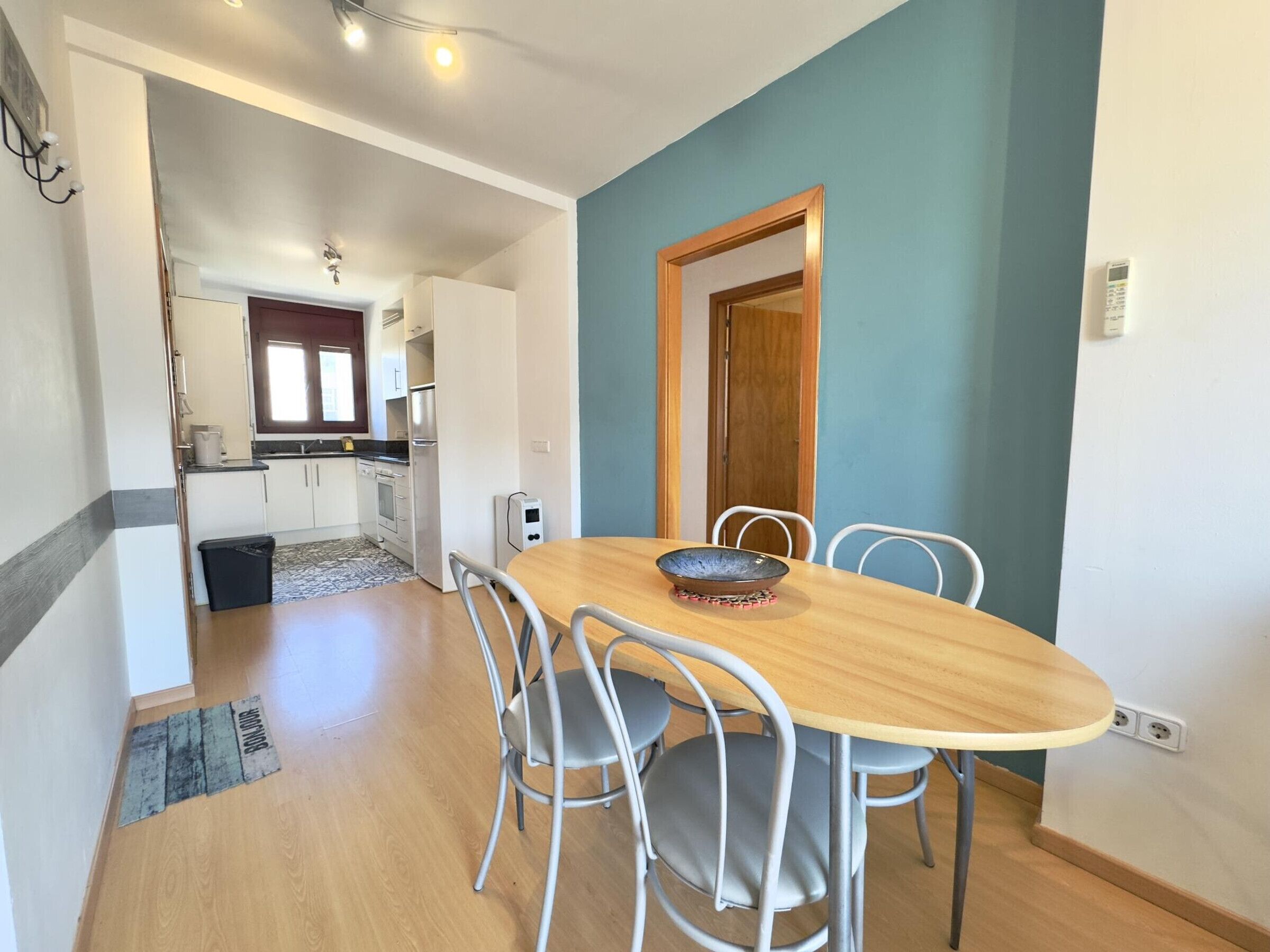 Zona pranzo con tavolo in legno e sedie in metallo, cucina sullo sfondo e parete decorata in blu.