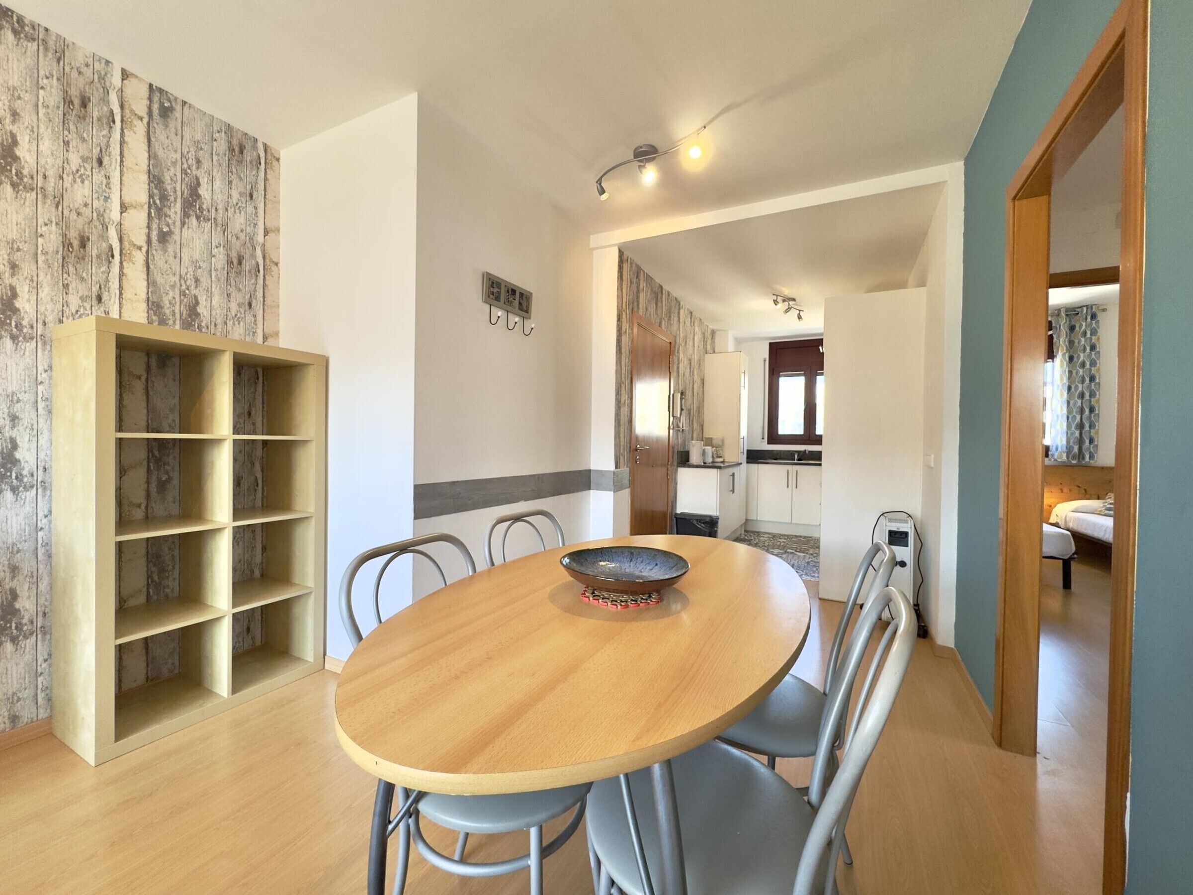 Un'area pranzo con tavolo e sedie in legno, una libreria a muro e vista sulla cucina e un'altra stanza.