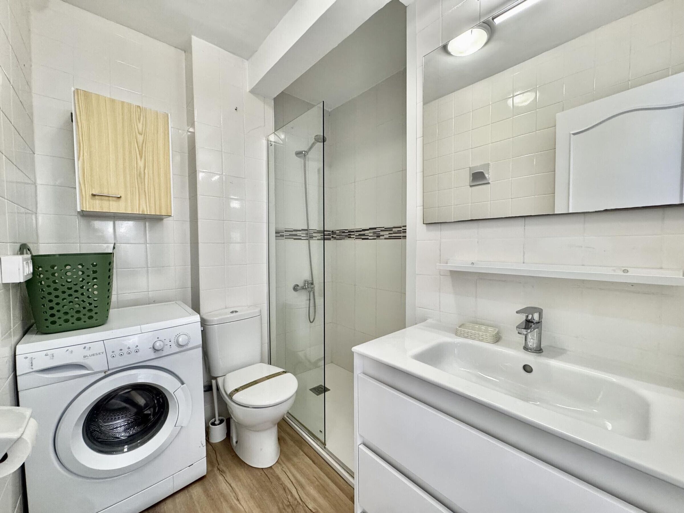 A modern bathroom with a washing machine, toilet, shower, and sink.