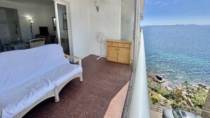 A balcony with a bed, a fan, a wooden cabinet, and a view of the sea. - 2-bedroom apartment with pool, parking, and WiFi near the beach in Roses (Roses)