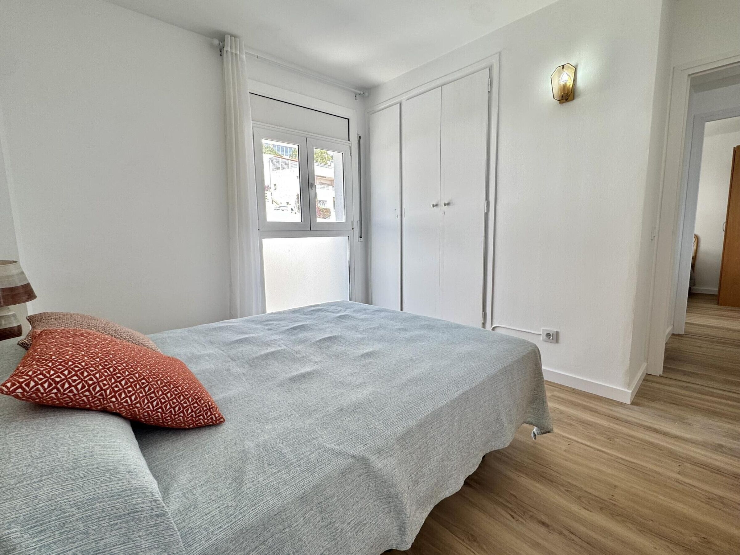 A bedroom with a bed, a window, a door, and a light fixture.