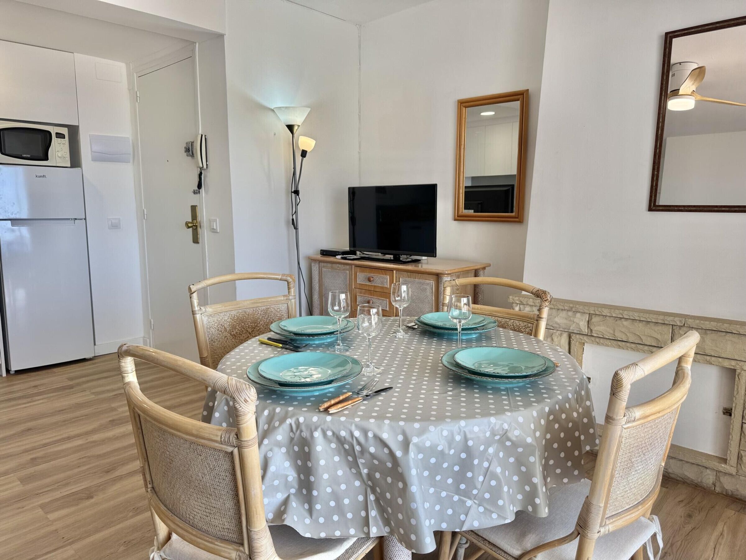 A dining area with a round table, four chairs, a television, and a microwave in the background.