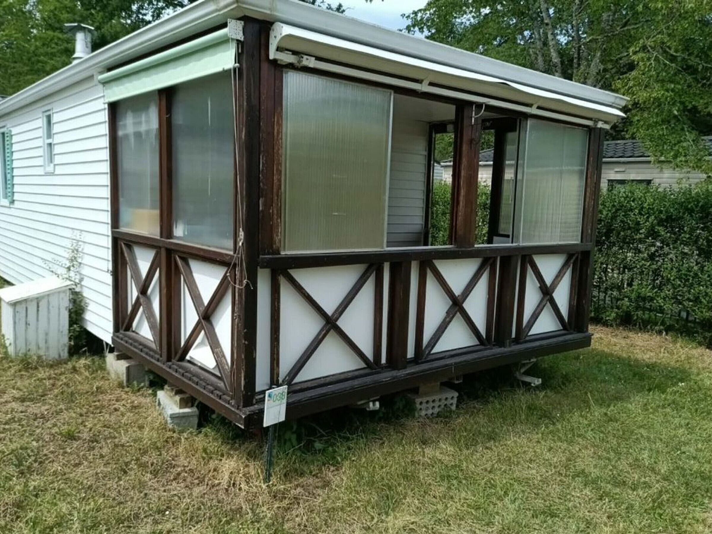 Ein Wohnmobil mit überdachter Veranda, großen Fenstern und einer kleinen Terrassenfläche.