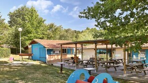 A playground with a blue car play structure, picnic tables, and a small building with a red roof. - Mobile home with terrace - 6 guests (Thiviers)