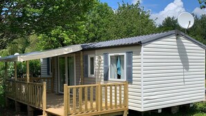 A mobile home with a wooden deck, a satellite dish, and a covered porch. - Mobile home with terrace - 6 guests (Thiviers)