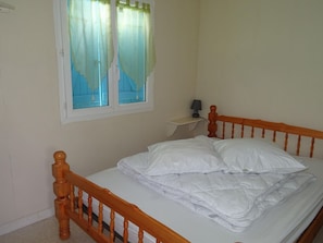A single bed with a wooden headboard, a bedside table with a lamp, and a window with curtains.