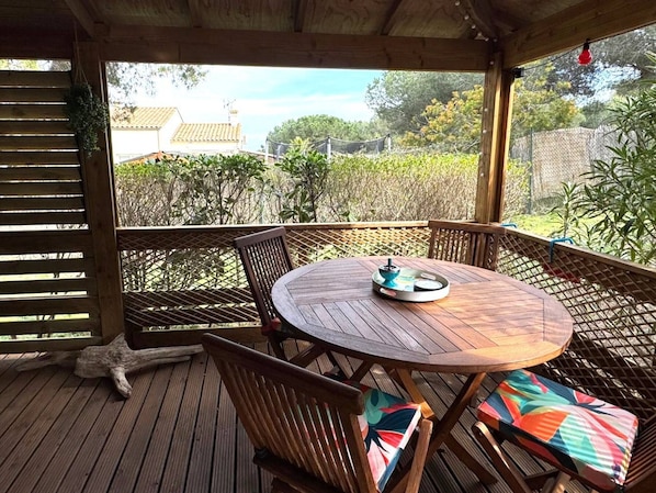 A wooden deck with a round table and chairs, a hanging plant, and a view of a residential area with trees and houses.