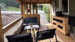 Ett avskärmat utomhusområde med sittplatser, bestående av en träbänk, två bord och stolar.