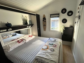 A compact bedroom with a bunk bed, a small window, and a surfboard decoration on the wall.
