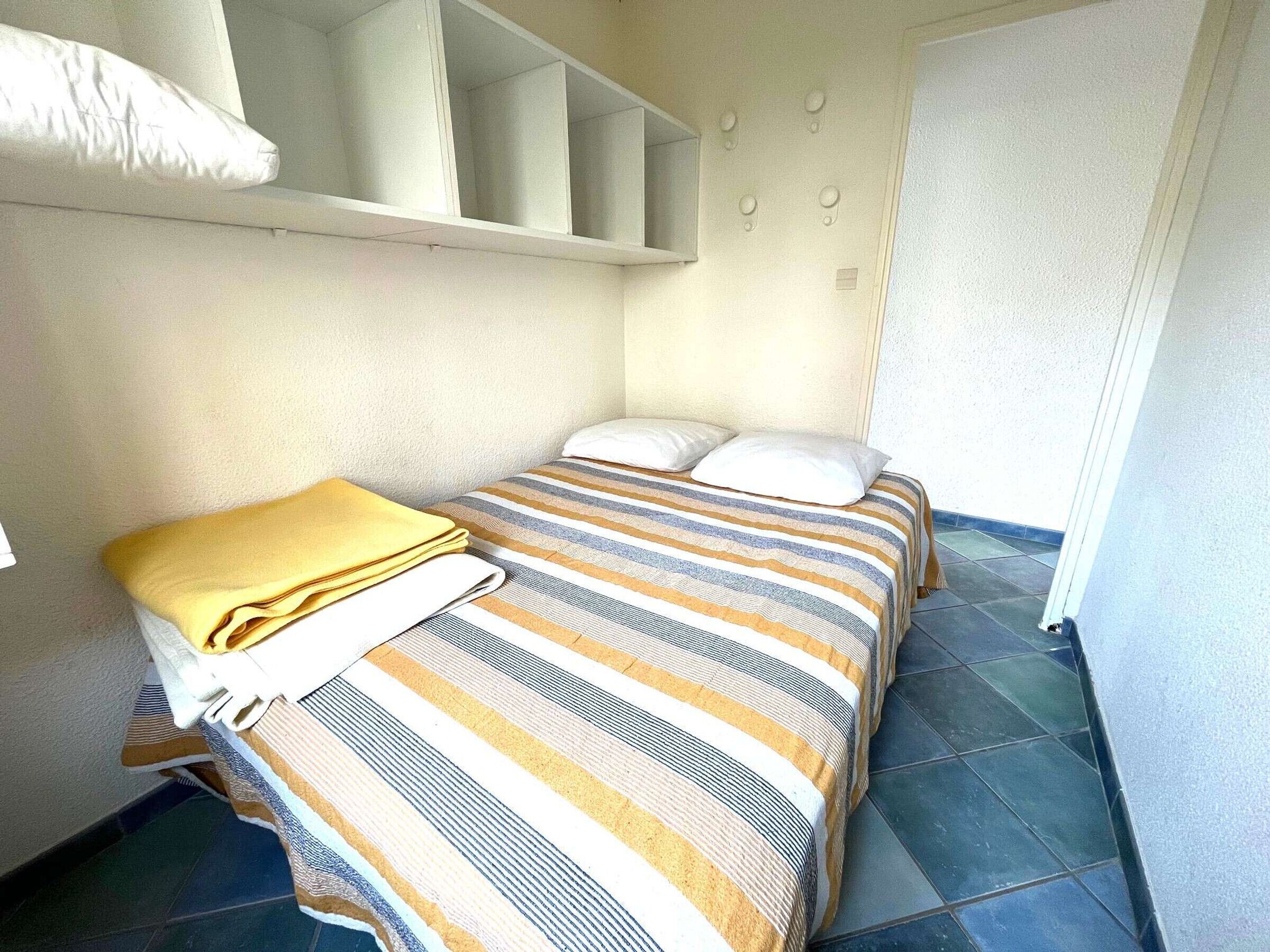 A small, neatly arranged bedroom with a striped bedspread, a yellow blanket, and a white pillow.